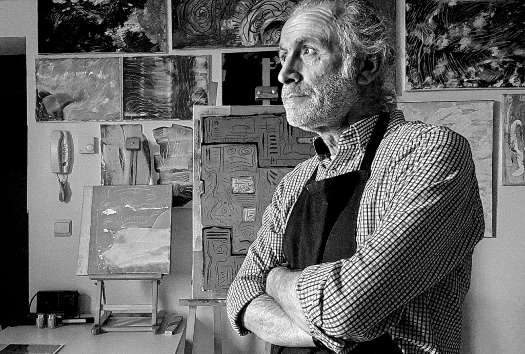 Hakan Portakal est à droite dans la photo, en tablier, les bras croisés, regarde vers la gauche d’où l’éclairage vient. Derrière lui, au mur en face, des tableaux abstrais accrochés.