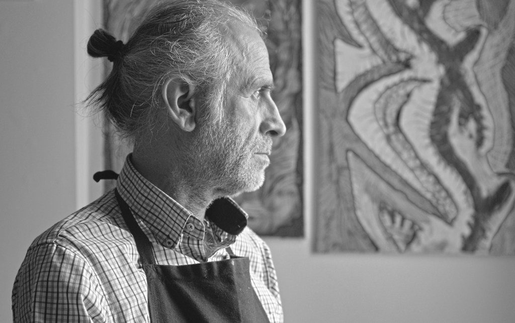 C’est un plan poitrine. Hakan Portakal est à gauche, distrait, regarde dans les sens ou vient la lumière et derrière lui, il y a deux tableaux abstraits accrochés au mur. 