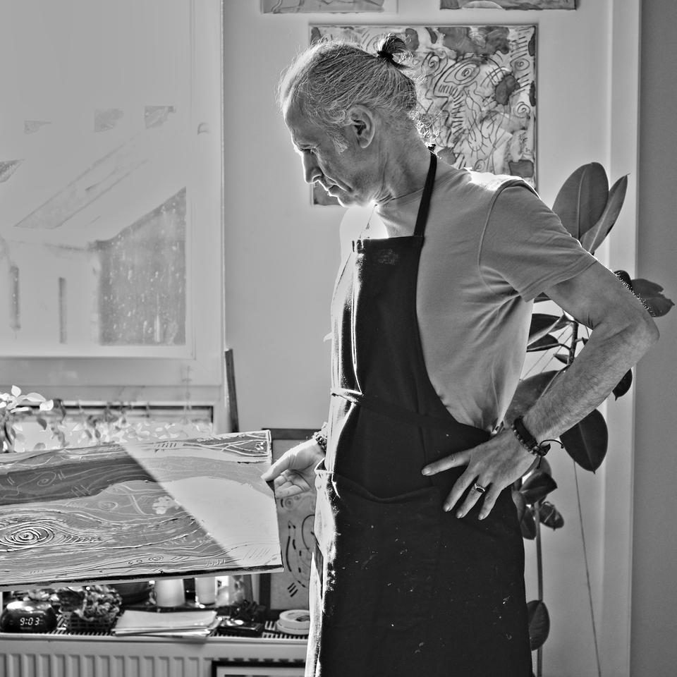 Hakan Portakal, dans son atelier, devant la fenêtre, légèrement tourné vers la gauche, tenant un tableau de la main droite, la main gauche sur la taille.