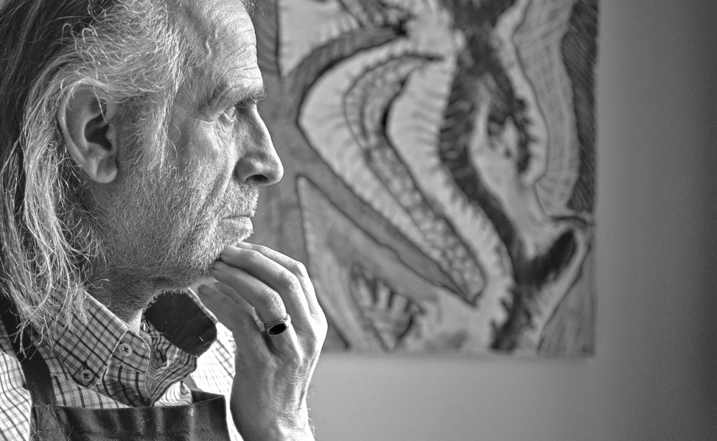 Sur la photographie, Hakan Portakal est à gauche, un portrait pris de la droite, on ne voit presque que son visage, longs cheveux gris, barbe de trois jours, chemise et tablier, les doigts de la main gauche sur le menton, pensif. Une peinture abstraite est accrochée au mur opposé. 