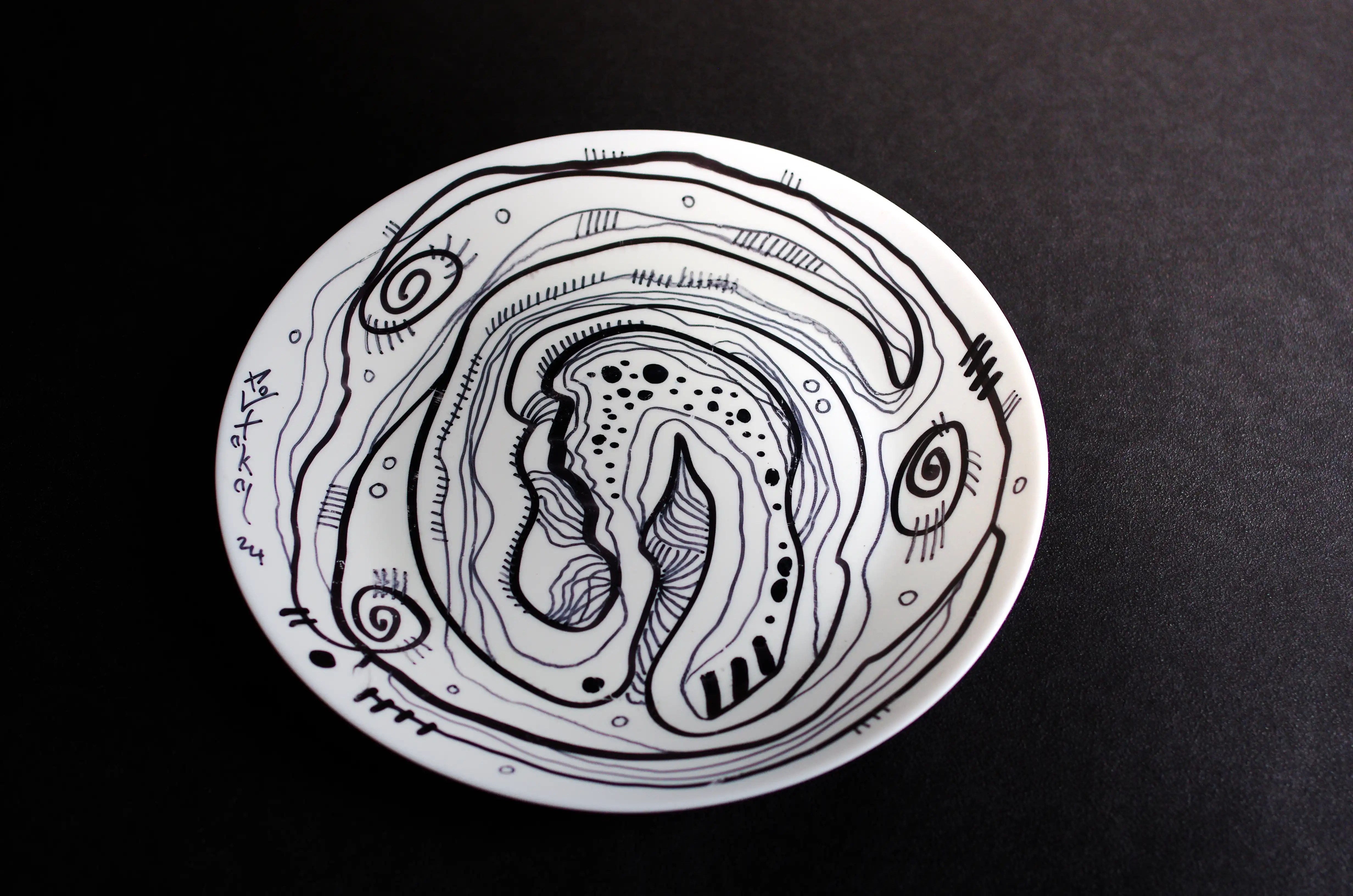 Une assiette circulaire blanche décorée de lignes noires courbes entrelacées. Chaque ligne est décorée de lignes dans la direction opposée. Trois spirales sont réparties sur trois côtés de l’œuvre. Vers le centre, les lignes s’intensifient et prennent de nombreuses autres formes. Il s'agit d'une œuvre d'art contemporaine et originale d'une qualité artistique extrêmement élevée. hakanportakal.com : clair, original, de bon goût… Un investissement intelligent.