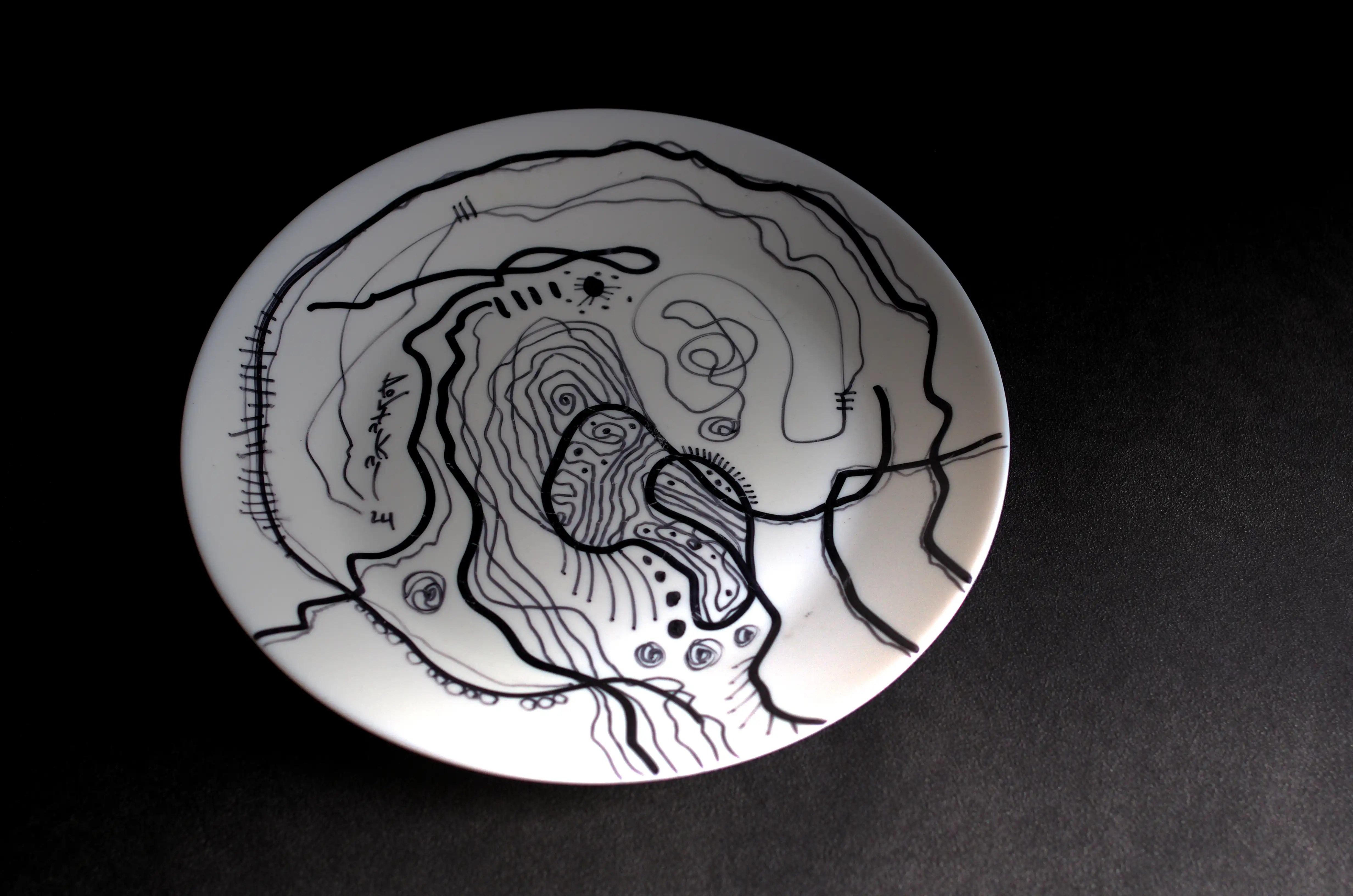 L’une de mes décorations d’assiette la plus chaotique. Des lignes noires onduleuses entrecroisées sont un peu partout sur ce travail exceptionnel. Une ligne épaisse travaillée entoure l’assiette et une autre débute par la gauche, en bas et remontre vers le haut. Le centre de l’assiette remplie de lignes onduleuses entrecroisées. C’est une assiette esthétique bien que sa décoration soit irrégulière. C’est une œuvre d’art moderne et originale de qualité. Osons la singularité. Décorez fièrement votre maison, votre bureau et vos meubles avec mes œuvres d'art de qualité et de valeur.