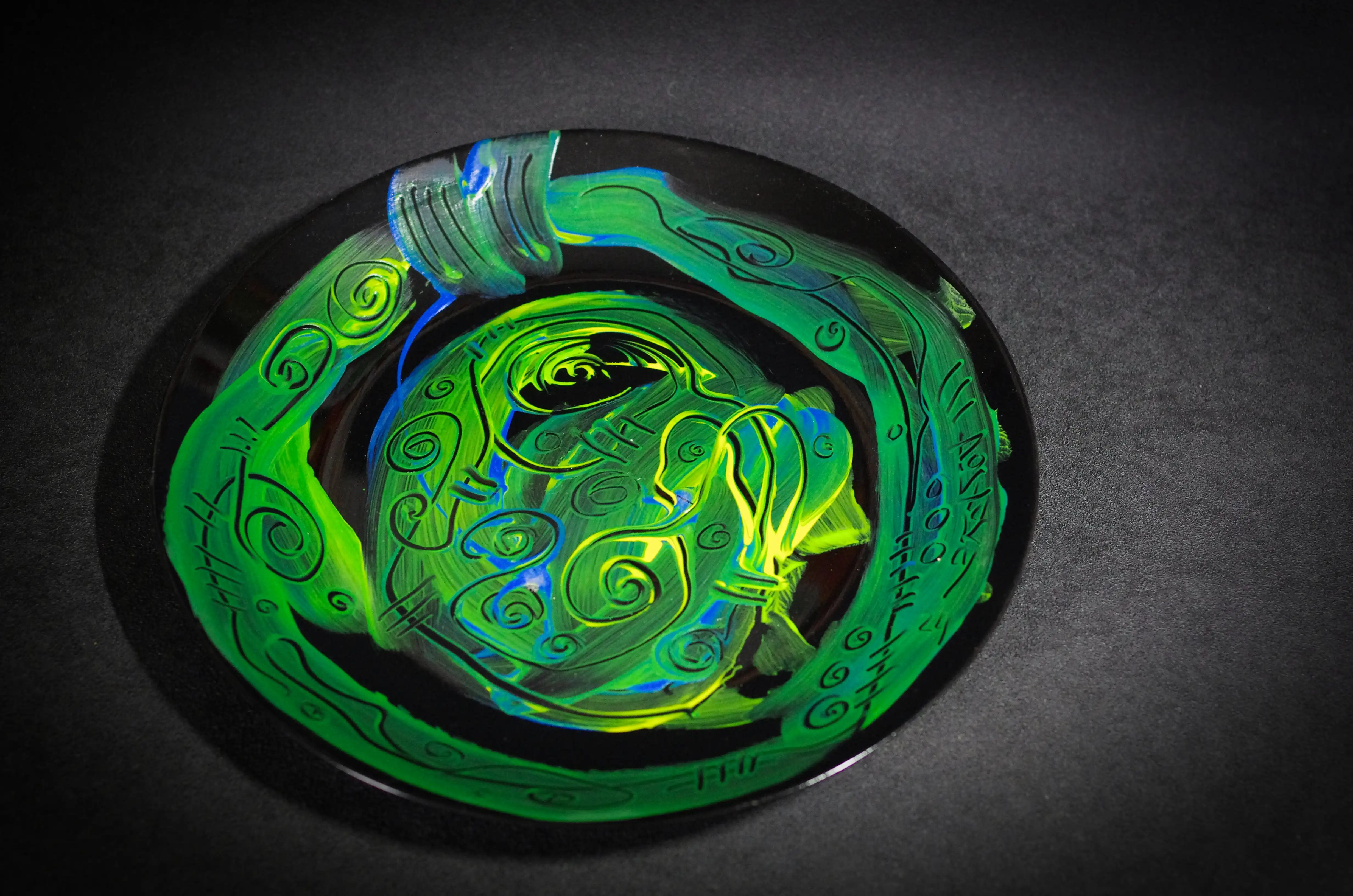 Cette très belle assiette noire est décorée à la peinture acrylique verte d'une manière à la fois brute et esthétique. Une section circulaire richement décorée se trouve au centre et les bords sont ornés d'une large bande de la même couleur. C'est un seul exemplaire qui occupe une place importante dans mon catalogue. Une œuvre d'art aussi précieuse et belle qu'une pièce de musée.
