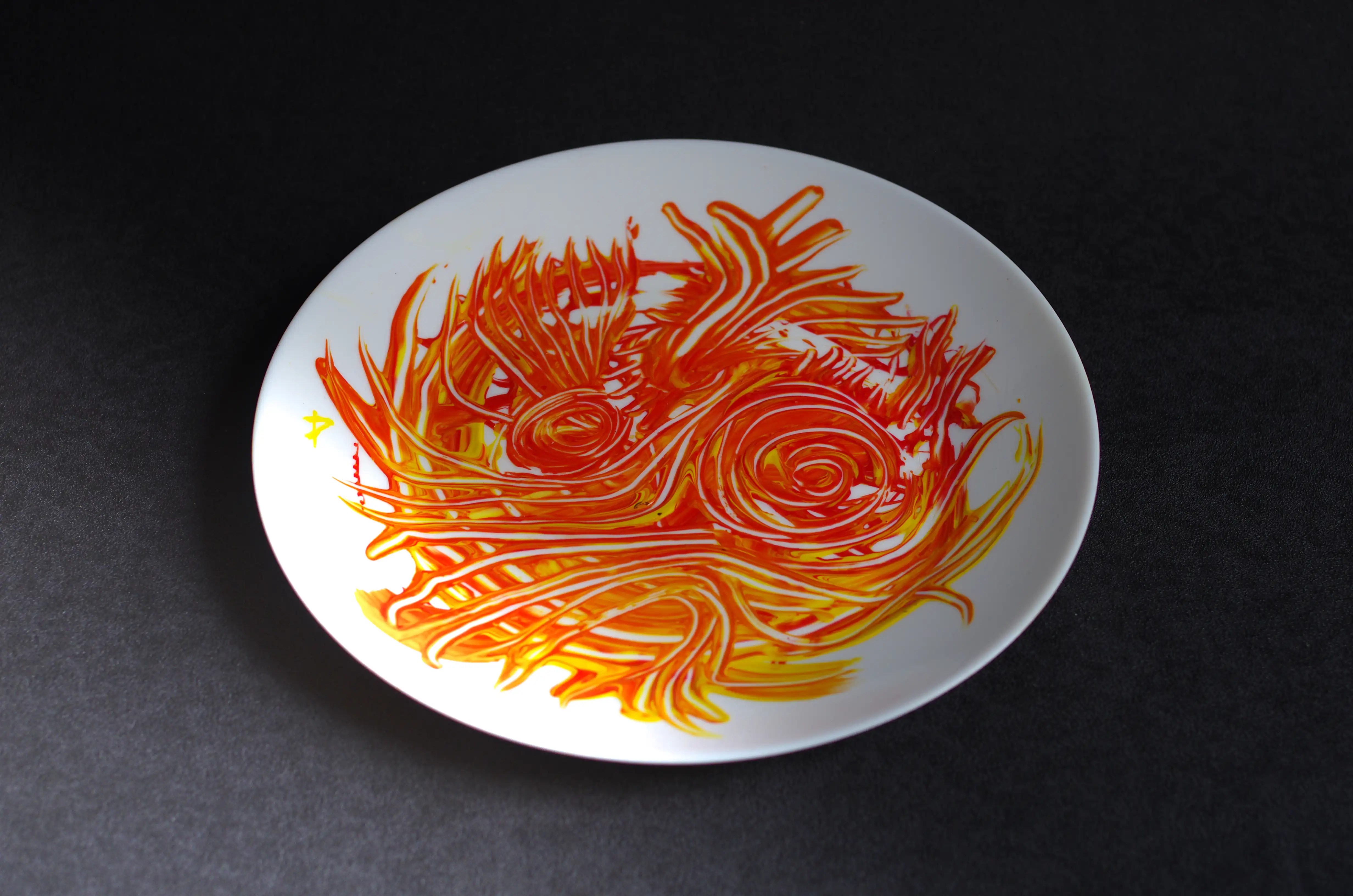 Les bords sont vierges et la décoration se trouve au centre. La peinture acrylique orange a été appliquée de manière aléatoire, puis travaillée en lignes courbes et entrecroisées pour créer des formes telles que des cercles et des courbes. 