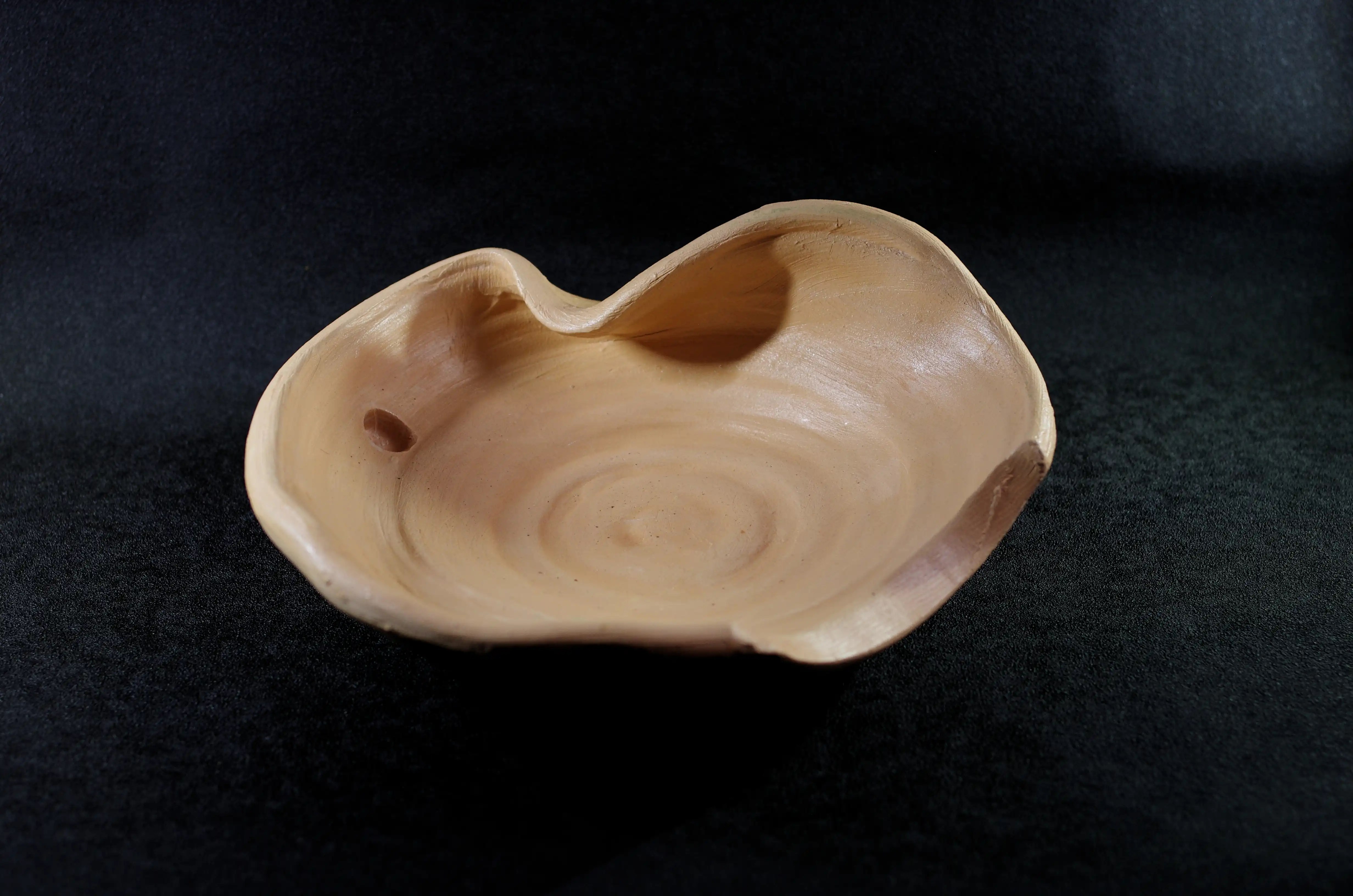 Il s'agit d'une pièce de poterie très classique, car elle n'est pas décorée (« nue » et de la couleur naturelle de l'argile), mais elle a une forme très inhabituelle. Elle est légèrement creuse. La hauteur des côtés est légèrement irrégulière et la partie la plus haute est incurvée vers l'intérieur. Une autre partie du bord est aplatie avec une découpe en forme de croissant. Il y a un trou près du bord incurvé. Les cercles formés lors du tournage sont visibles à la base. La couleur de cette jarre est beige, la couleur originale de l'argile. Elle est vernissée comme mes autres céramiques. Osons la singularité. Achat en toute sécurité. 
Esthétisez votre argent.